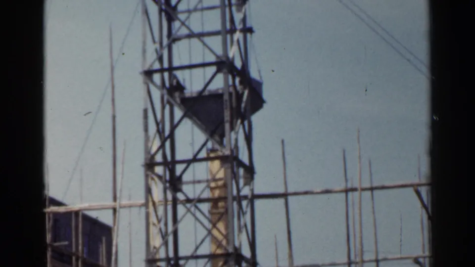 1953 Japan 8mm frame showing the upper portion of a steel lattice tower with diagonal bracing, platform details, and guy wires.
