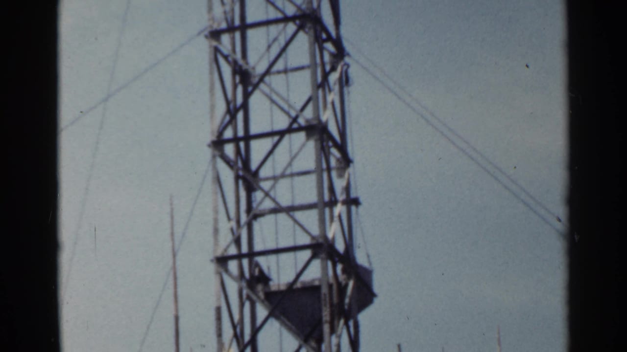 1953 Japan home-movie frame of a steel tower rising through the frame, with guy wires crossing the pale sky.