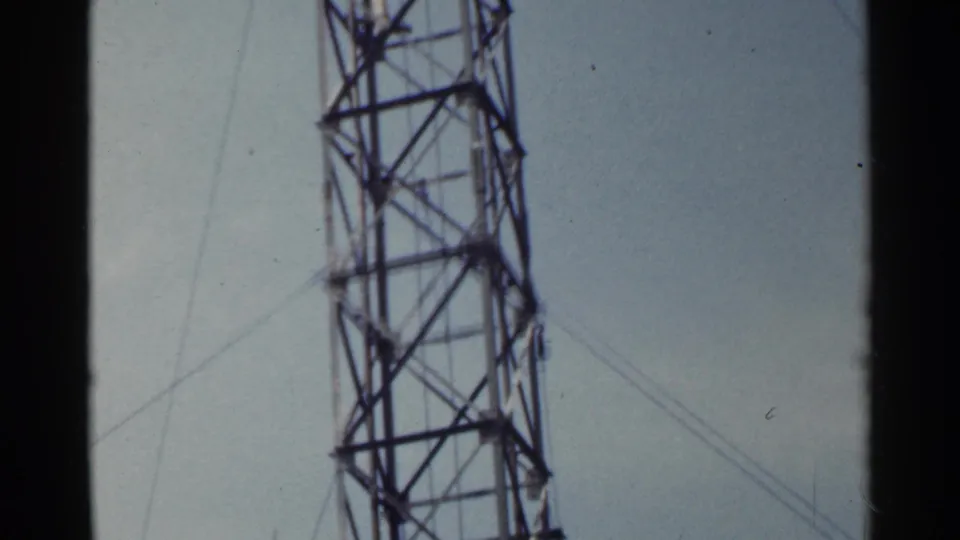 1953 Japan 8mm frame showing a closer view of the tower's lattice bracing and support wires against a muted sky.