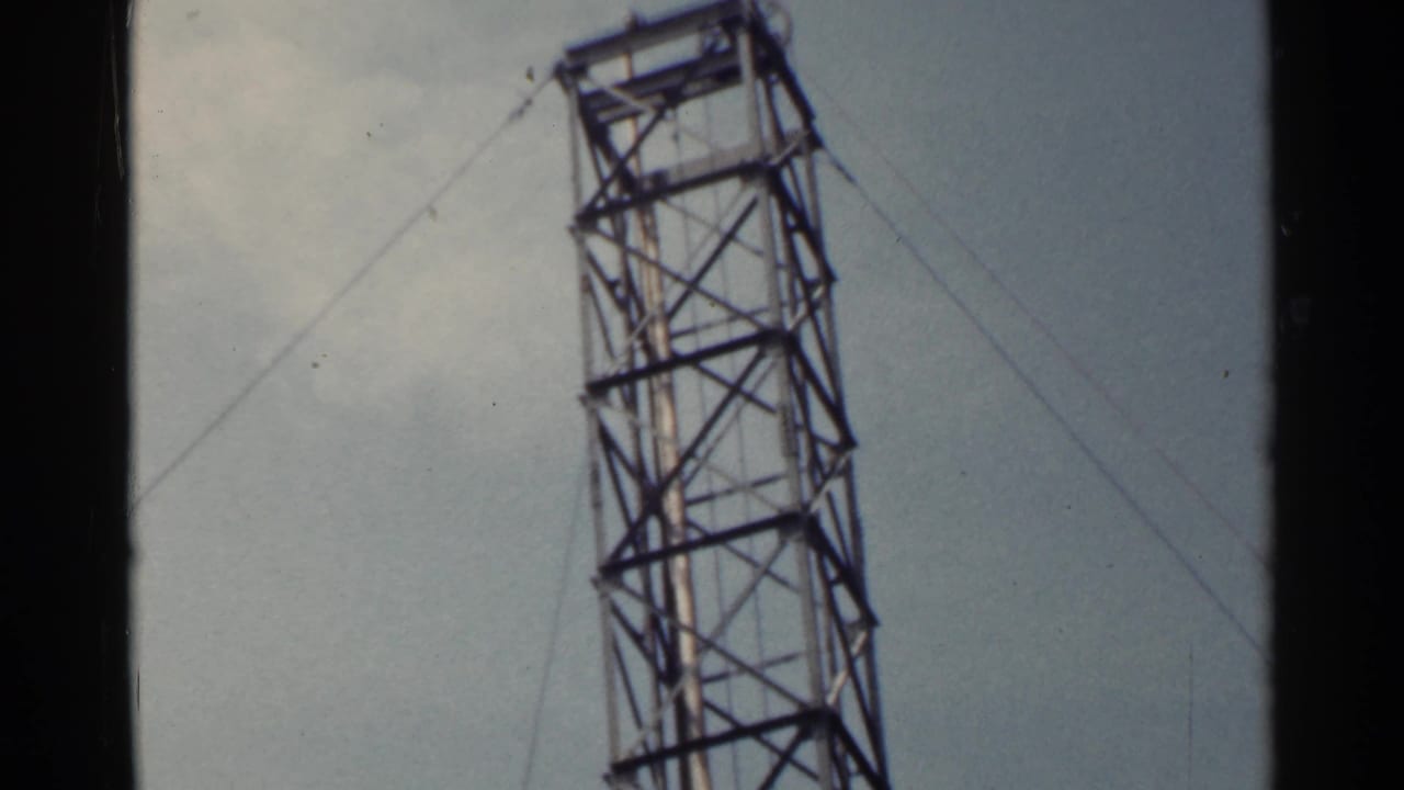 Angled metal tower with cables against a cloudy sky.