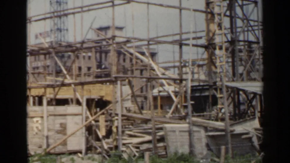 1953 Japan frame showing a construction site with timber scaffolding, exposed framing, and a tower at the side.