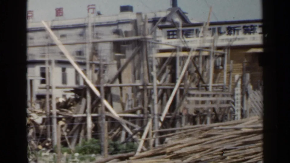 1953 Japan construction frame with Japanese signage on a small site hut, scaffolding, and stacked wood in front.