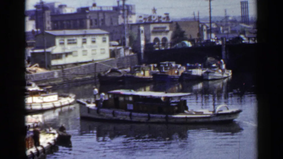 1953 Japan canal view with small boats, a larger houseboat-like vessel, industrial buildings, utility poles, and water reflections.