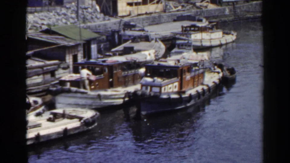 1953 Japan harbor view with small wooden boats tied together near the quay and a worker visible on a deck.