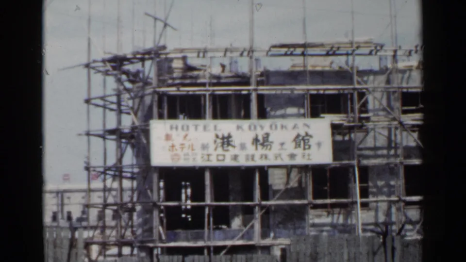 1953 Japan home-movie frame of scaffolding around an unfinished hotel facade with Hotel Koyokan lettering and Japanese text.