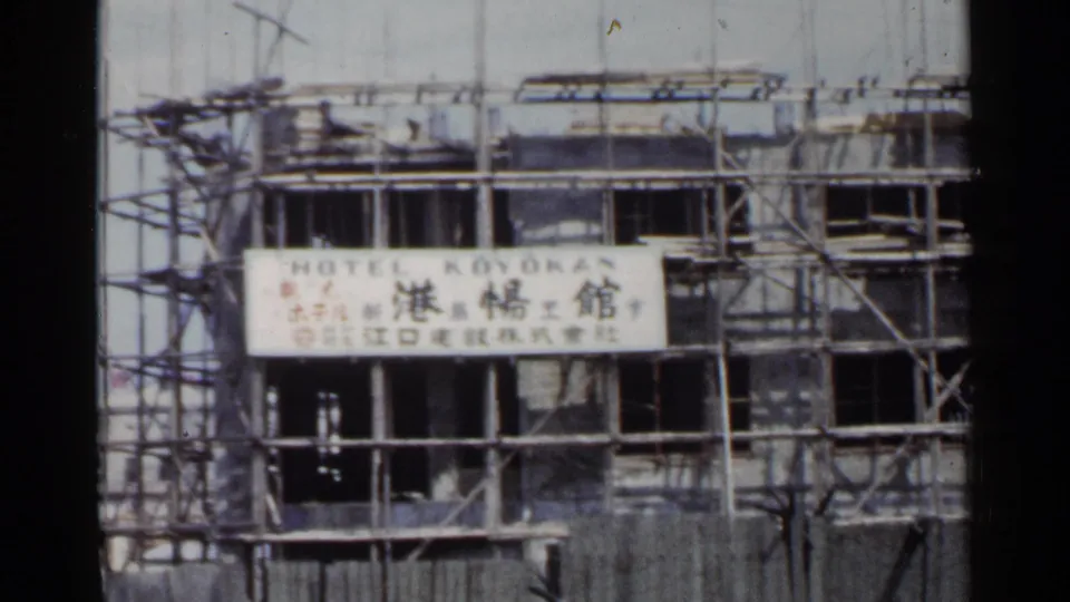 1953 Japan 8mm frame showing the Hotel Koyokan construction sign across scaffolding, with open bays and framing visible.