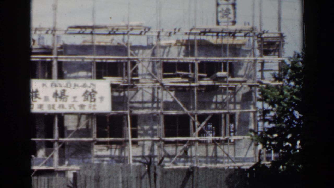 1953 Japan 8mm frame showing a multi-story building under scaffolding with Japanese signage on the facade.