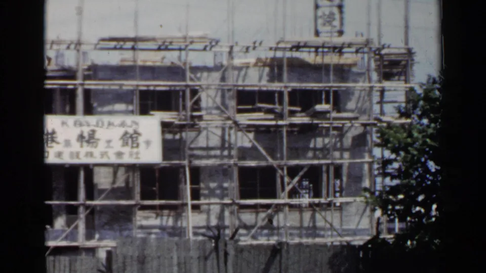 1953 Japan 8mm frame showing a multi-story building under scaffolding with Japanese signage on the facade.