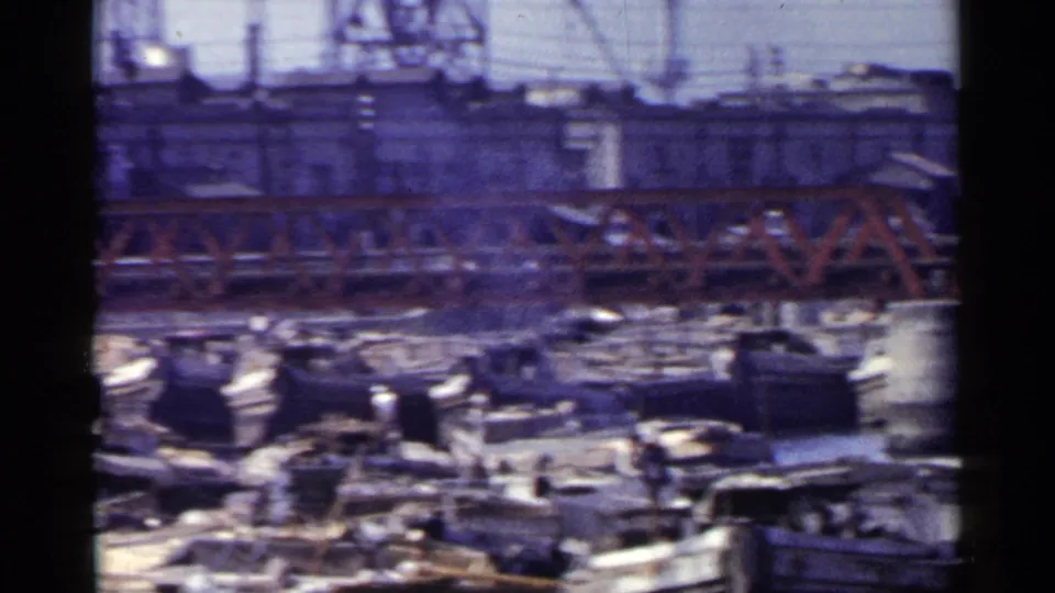 1953 Japan frame showing many small craft and barges packed along the water beneath a red truss bridge and industrial buildings.