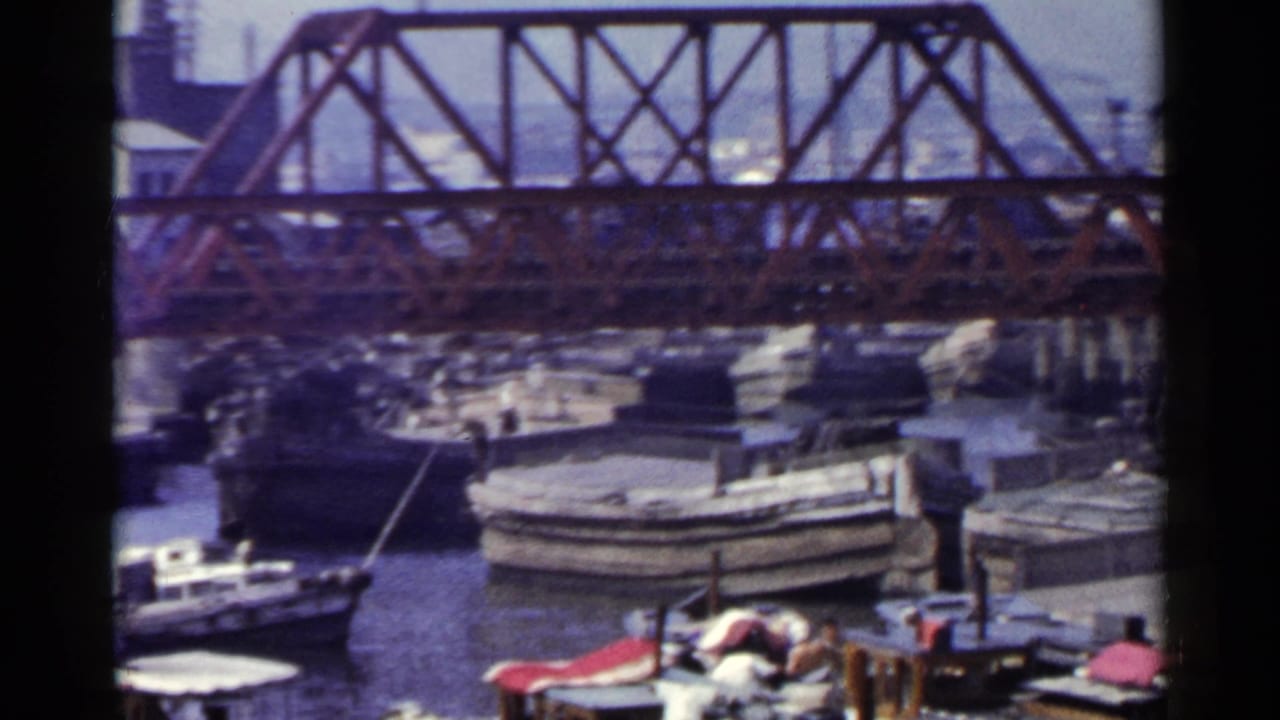 Small boats clustered near a red truss bridge over a harbor.