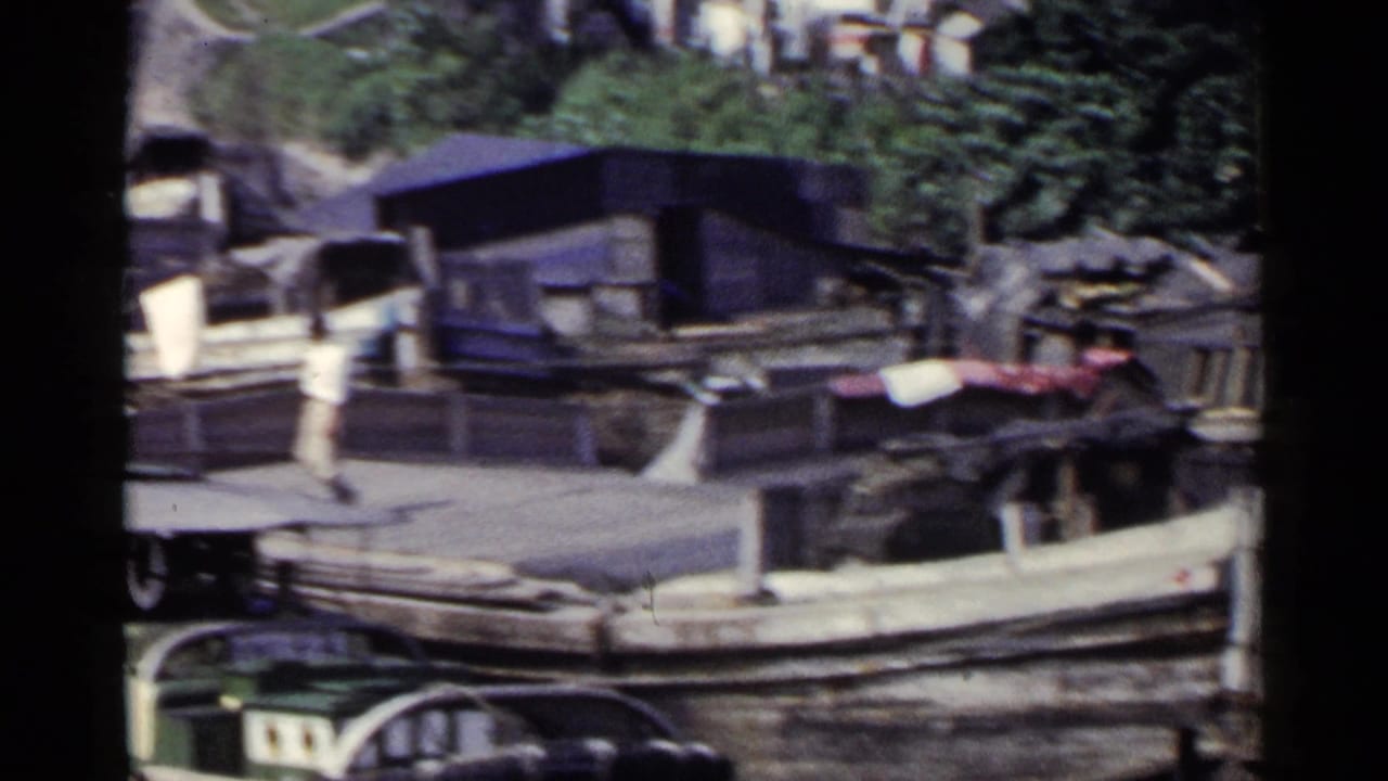 Wooden boat moored beside a riverside dock with waterfront buildings behind it.
