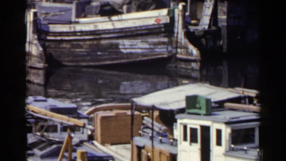 Japan 1953 waterfront frame showing a larger wooden boat and a smaller cabin boat beside weathered dock pilings.