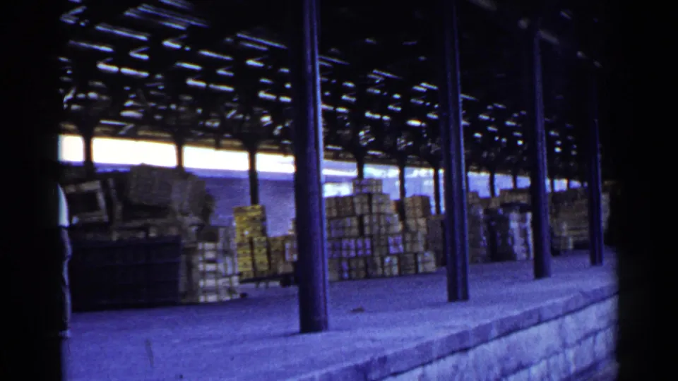 The covered dock remains in view with stacked crates, metal columns, and a partially visible worker at the left edge.