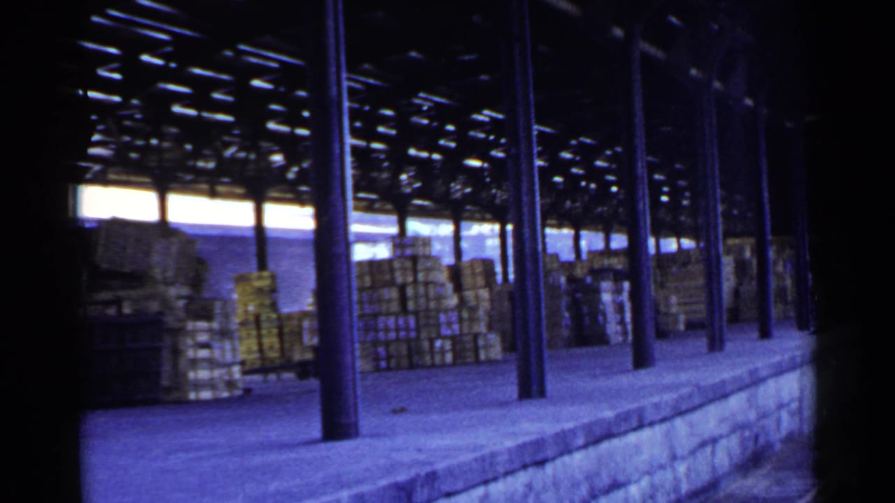Covered rail loading platform with stacked crates and dark metal columns.