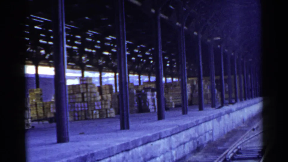 1953 Japan rail freight scene with crates under a shed roof and dark columns receding along the platform.