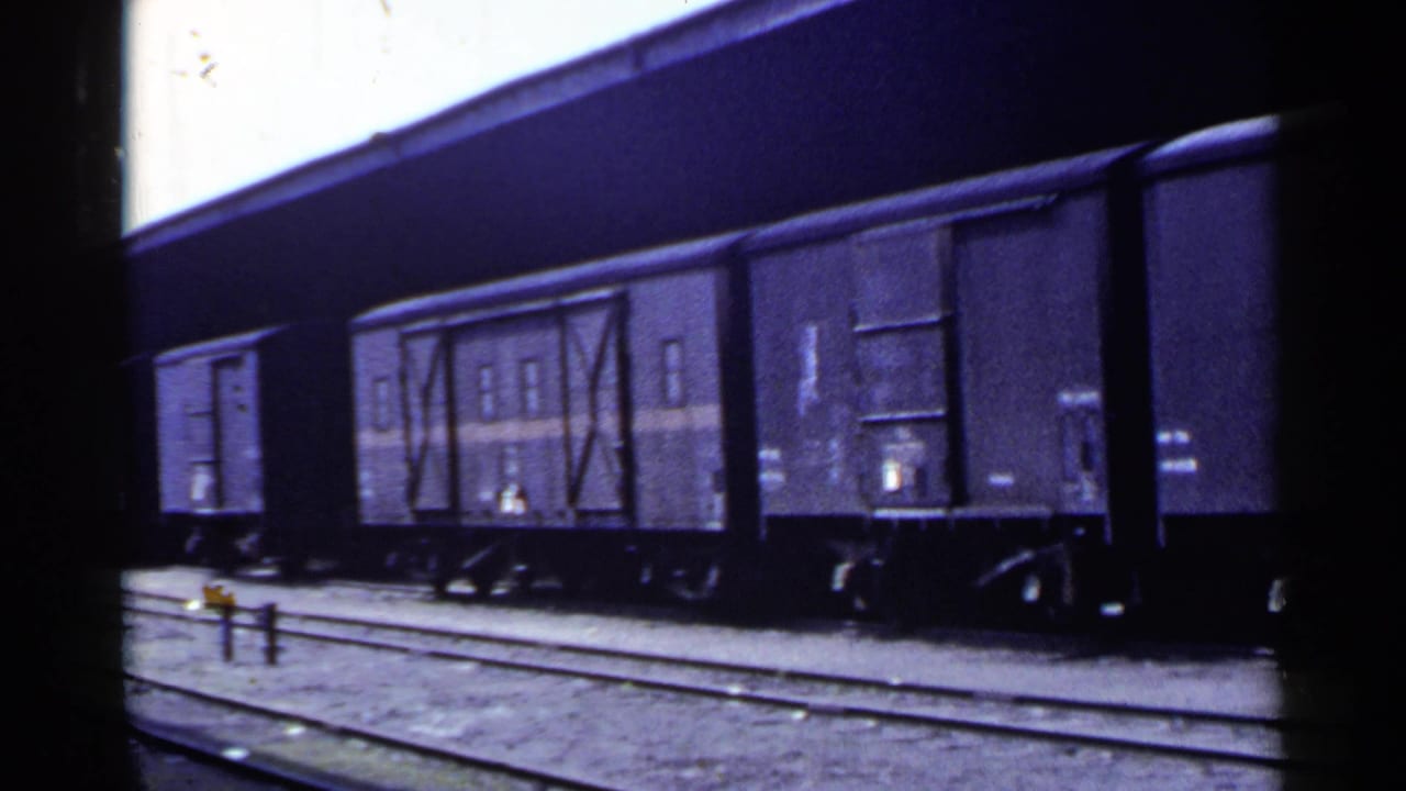 1953 Japan 8mm frame with stopped freight wagons, sliding doors, undercarriage wheels, and rail tracks in view.