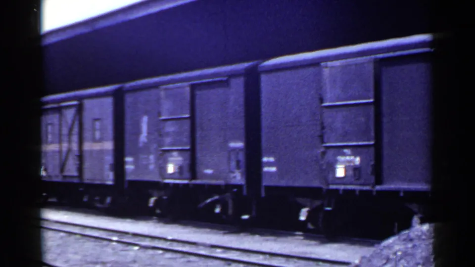 1953 Japan 8mm frame showing the side of stopped cargo wagons with doors, wheels, rails, and gravel ballast.