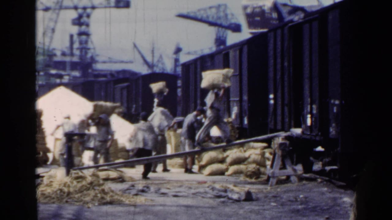 1953 Japan footage shows workers carrying burlap sacks near open freight cars, with cranes and piled cargo in the background.