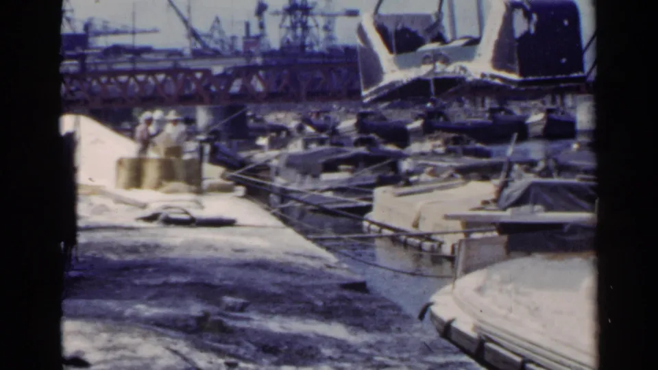 The 1953 Japan port scene shows a suspended crane bucket above boats and dockside water, with industrial cranes and structures beyond.