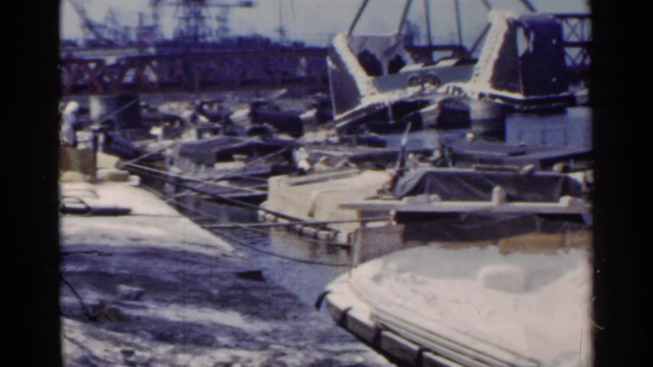Crane over a white-loaded barge with boats and a truss bridge in the background.