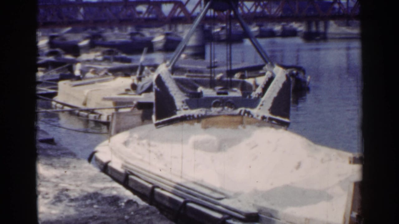 1953 Japan 8mm still showing the crane structure and a white-loaded barge from a slightly shifted harbor viewpoint.