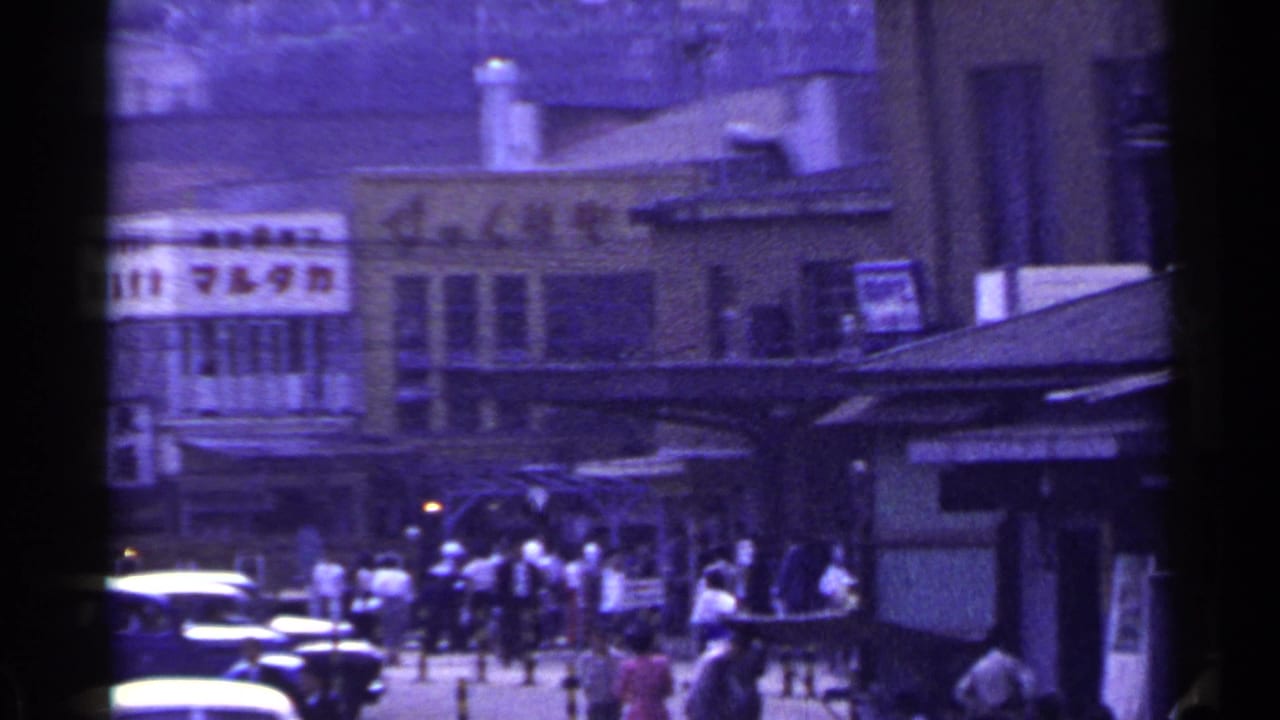 Busy Japanese commercial street with pedestrians, cars, and shop signage.