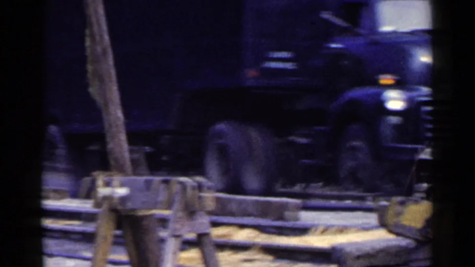 A dark truck moves past a Japanese road construction area with sandbags, barriers, and timber or equipment visible in the foreground.