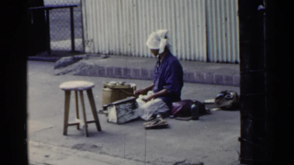 A 1953 Japan street view shows the woman seated near a low stool and basket, with tools and bags arranged around her.