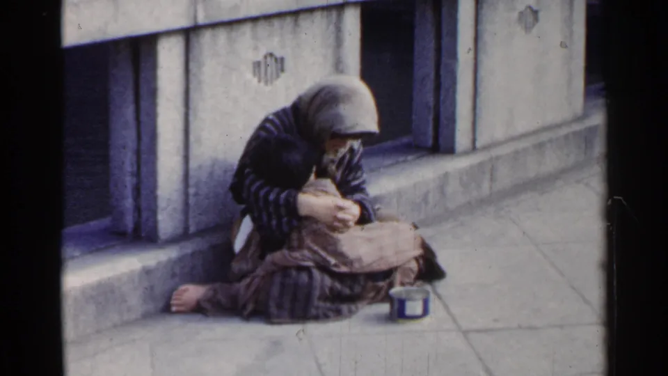 The 8mm frame shows a bundled person seated on a Japanese city bridge walkway, partly turned downward toward their lap.