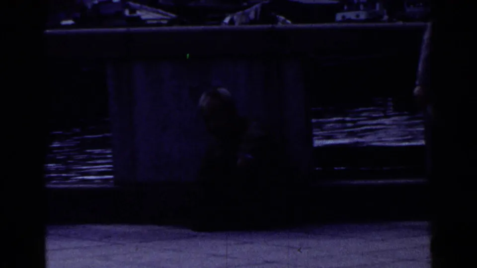 Dark 1953 Japan 8mm frame looking under or beside the bridge, with water, a concrete support, and a shadowed person partly visible.