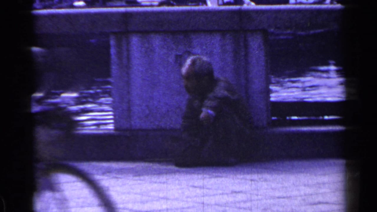 Seated man near a bridge pillar as a bicycle or vehicle blurs across the foreground.