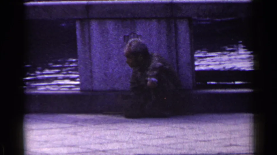 1953 Japan home-movie frame showing the man still seated near the bridge pillar, with water and film-edge shadows around the scene.