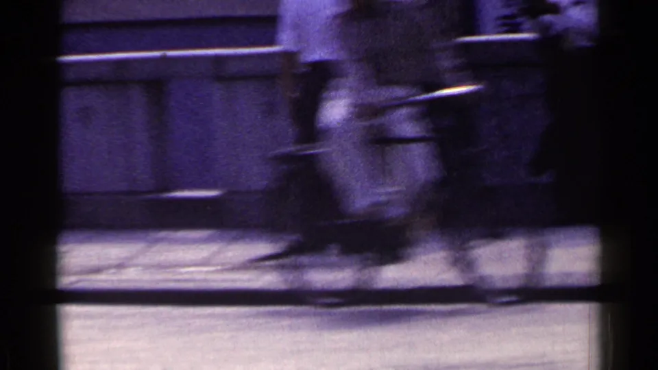 1953 Japan 8mm frame of pedestrians moving past a concrete wall, one carrying a light bag or case.