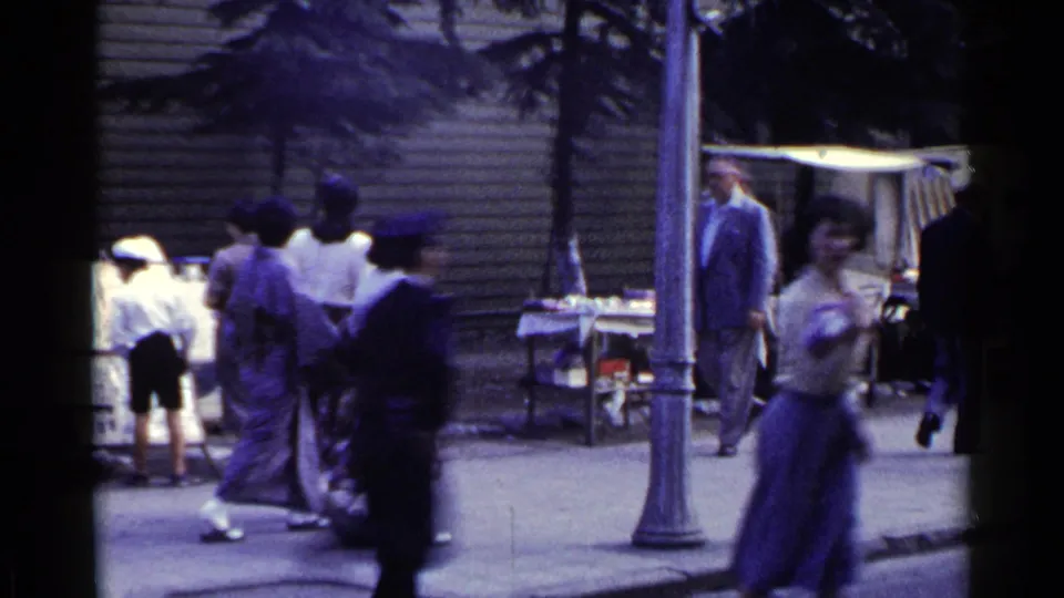 1953 Japan sidewalk scene with people walking past market tables, a lamppost, and wooden building fronts.