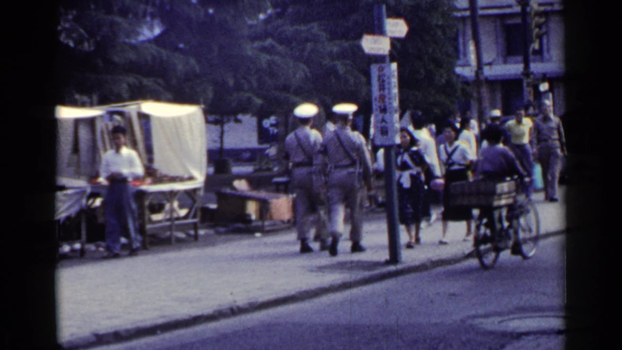Uniformed men and pedestrians pass a market stall while a cargo bicycle is nearby.