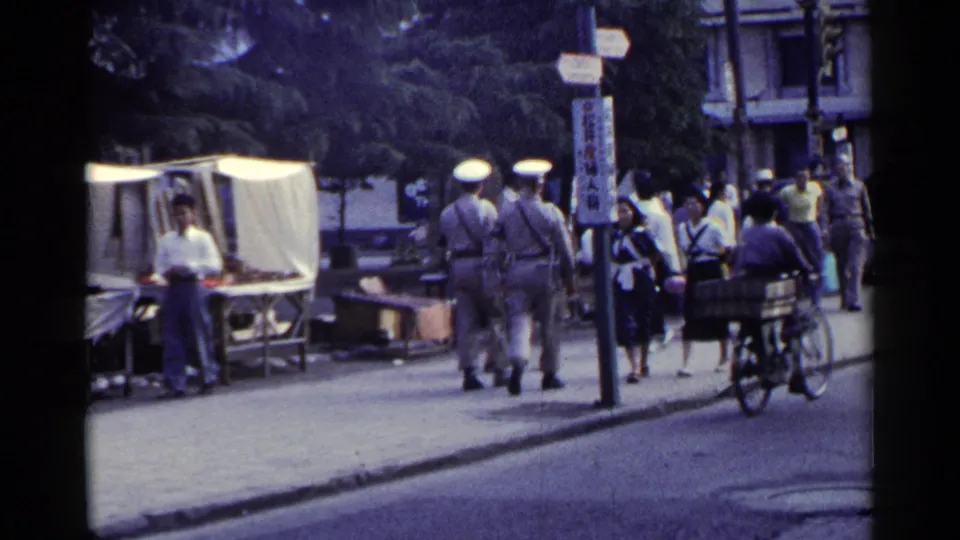 1953 Japan sidewalk scene with uniformed men, pedestrians, a white-canopied stall, vertical signage, and a cargo bicycle at the curb.