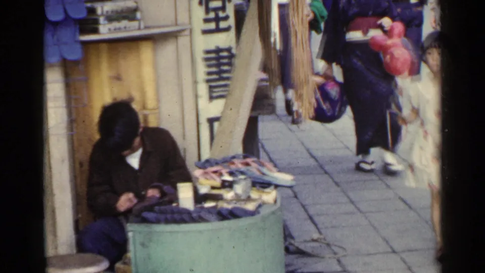 1953 Japan street-level view of a shoe repairman seated by a small display of footwear and repair items near vertical signage.