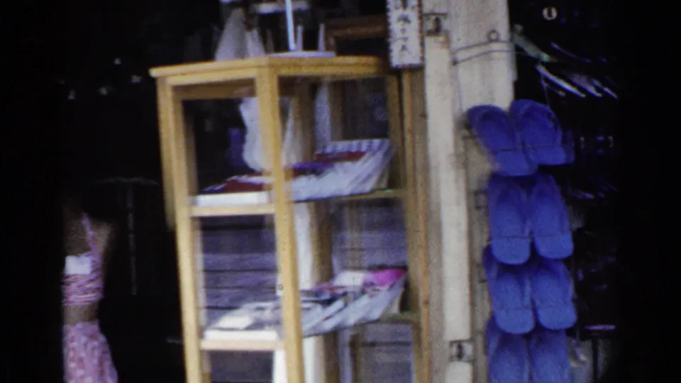 A wooden display case with papers or magazines stands near hanging blue sandals and shelves of footwear.