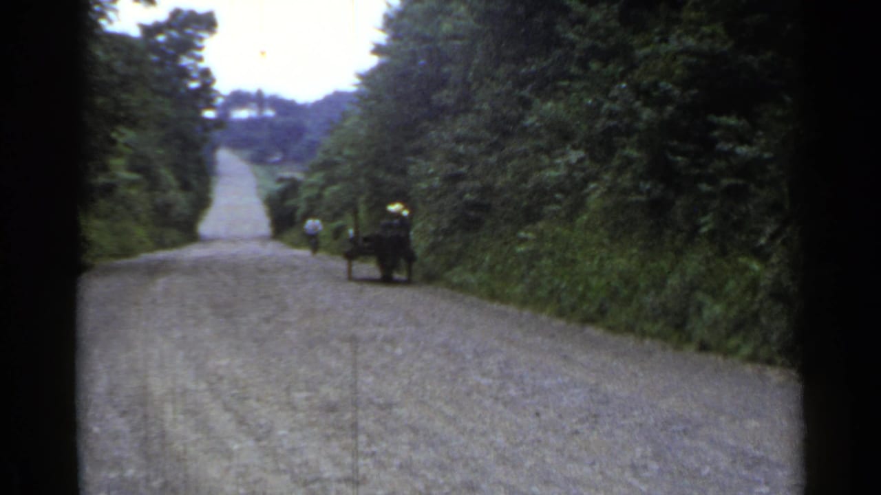 Distant figure and small cart on the right side of an empty gravel road.