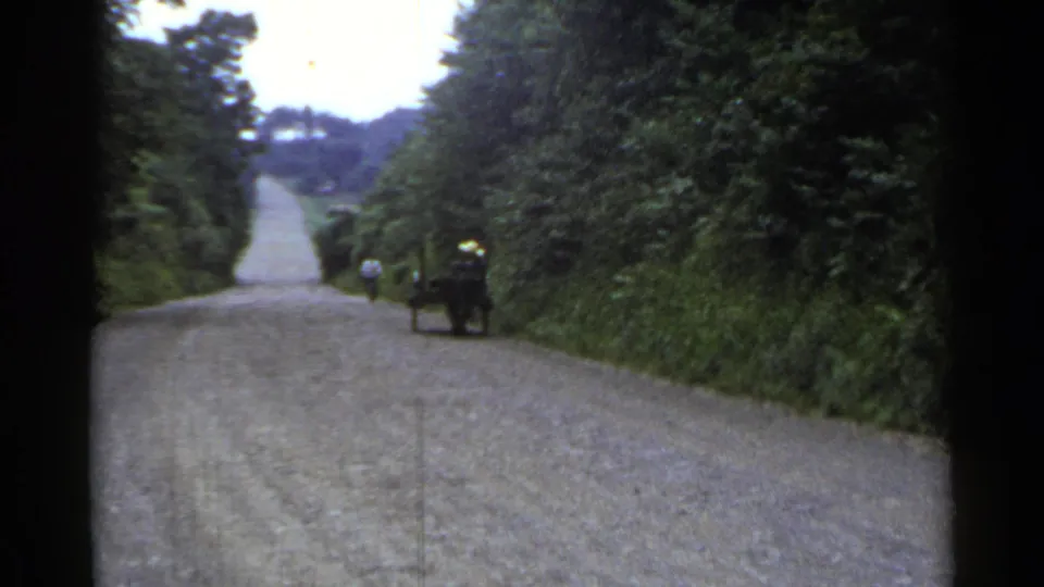 1953 Japan frame with a lone roadside figure pushing a small cart away from the camera on a tree-lined gravel road.