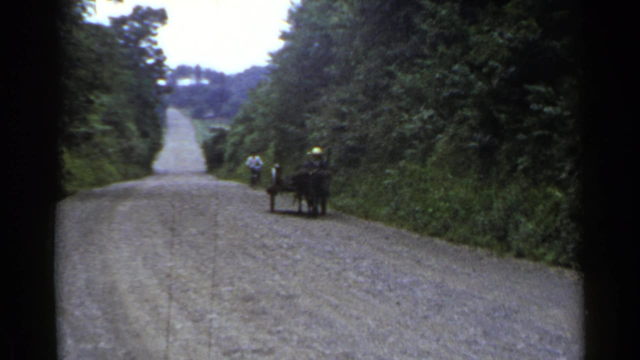 1953 Japan frame with a horse-drawn cart at the right edge of a rural road and a cyclist ahead in the distance.