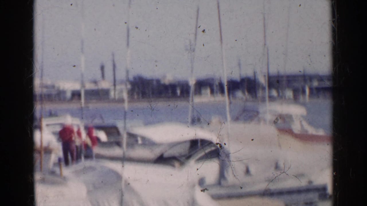 Docked white boats in a harbor with small distant people near the left side.