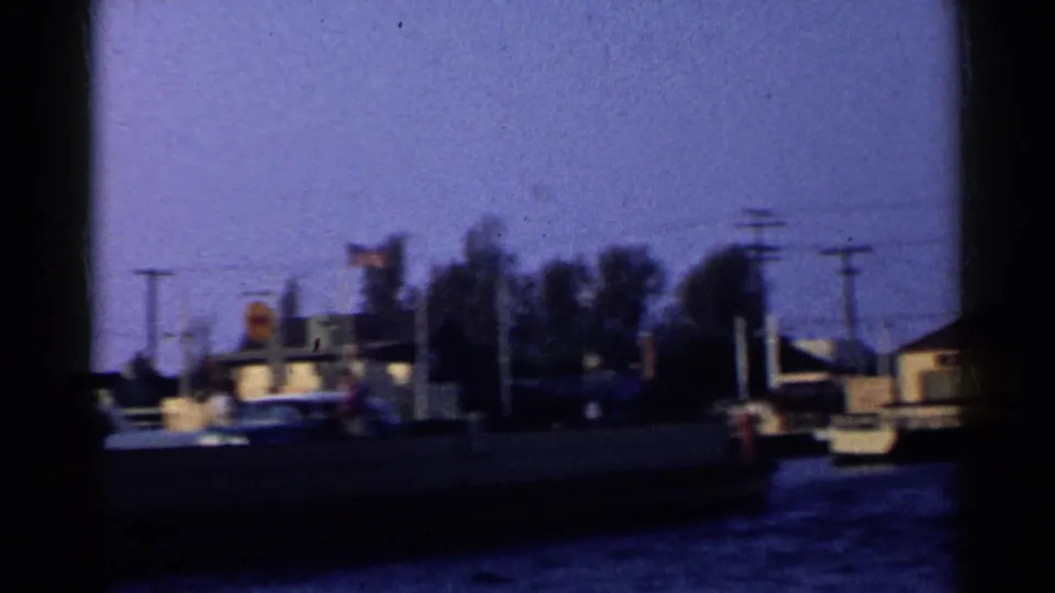 A dark-hulled boat crosses the harbor foreground, partially silhouetted against blue water and a tree-lined California shoreline.