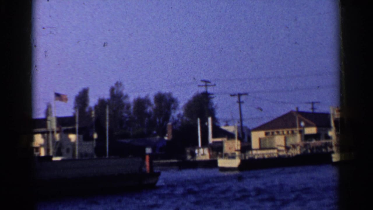 Boat-level view of waterfront buildings, water, utility poles, trees, and a small American flag.