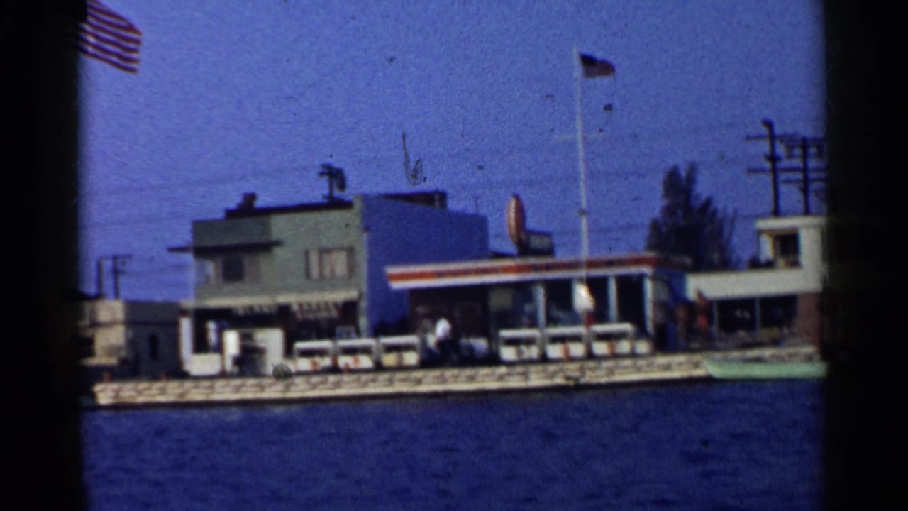 Waterfront buildings, flags, boats, and utility poles seen across blue harbor water.
