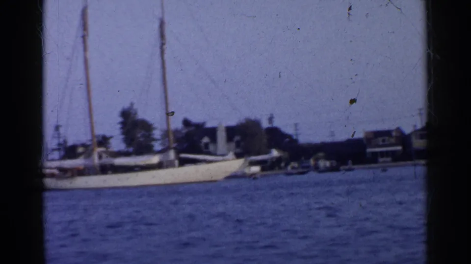 Soft 8mm frame of a California waterfront with sailboat rigging, small boats, houses, and utility poles.