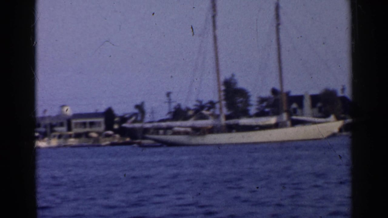 Harbor water with a docked sailboat and shoreline houses behind dark film borders.