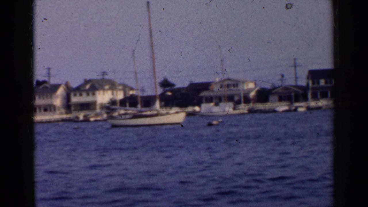 Waterfront houses and moored sailboats across rippling blue water.
