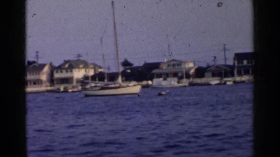 1955 California 8mm frame showing waterfront houses, docks, and sailboats viewed from across a waterway.