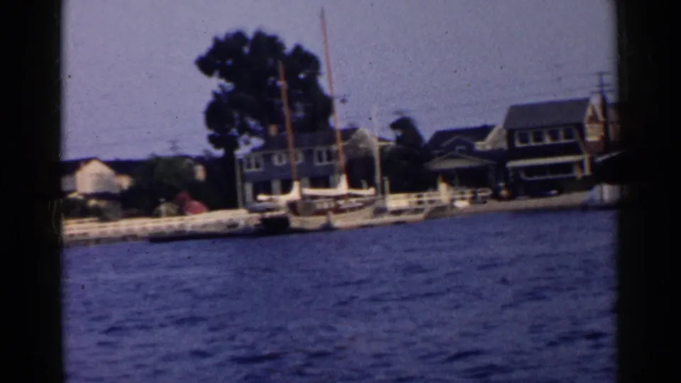 California 1955 home-movie view of houses and trees along the shore, with small boats tied at docks.